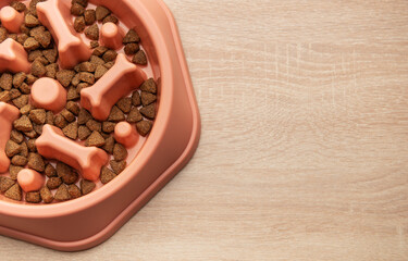 Dry dog food in slow feeder bowl on wooden surface