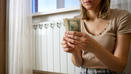 A woman sits calmly near a window, holding a bundle of cash in her hands. The warm light highlights her focused expression as she carefully counts the money.