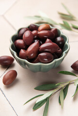 Kalamata olives with olive branches in a green bowl on a tiled surface