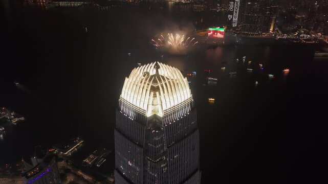 Drone shot of the IFC building at night with fireworks in the background in Hong Kong