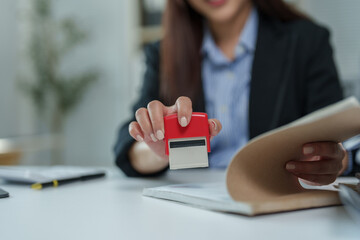 Businesswoman holding a stamp, preparing to approve an important document while seated at her desk in a corporate office, demonstrating professionalism and attention to detail