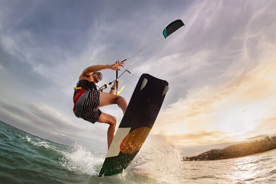 Kite surfer with wake board jumps close to camera at sunset sea beach. Closeup photo of athlete is jumping over camera