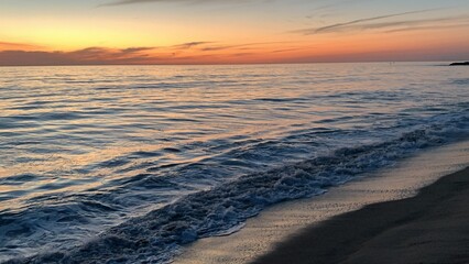 Obraz premium A color photo of calm ocean waters in Carlsbad, California, with gentle waves under a clear sky, bordered by a sandy beach.