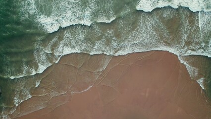 Top view of the seashore, foamy sea waves hitting the sandy beach