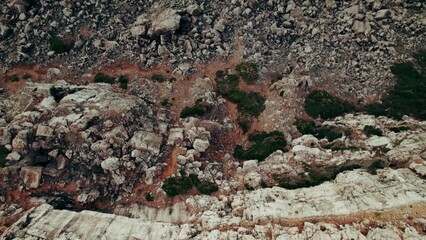The drone flies over the pebble beach to the sea, foam waves wash the rocks, top view