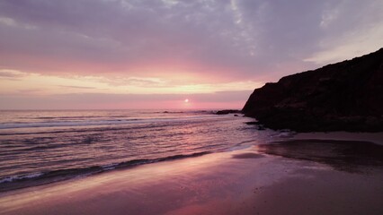 Drone view of the sea at sunset, sandy beach surrounded by rocky mountains
