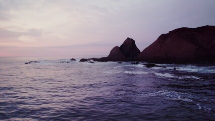 Seashore with rocky cliffs at sunset, drone flying over the water