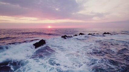 Obraz premium A bird's-eye view of the sea at sunset. Foam waves wash the stone reefs on the shore. Drone video