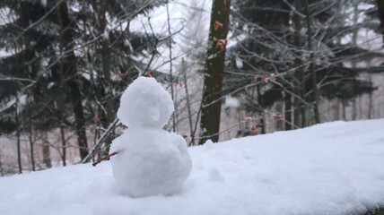 A charming little snowman crafted from snow, nestled in a serene, snow-covered forest during...