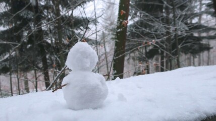 A charming little snowman crafted from snow, nestled in a serene, snow-covered forest during...