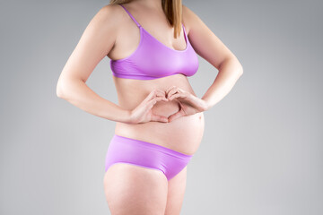 Pregnant woman with big belly in purple underwear on gray background, pregnancy concept