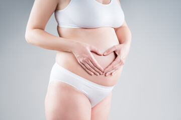 Pregnant woman with big belly in white underwear on gray background, pregnancy concept