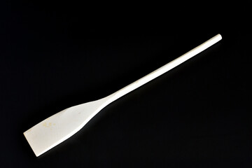 A new wooden spatula with a long handle lies on a black background.