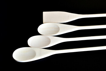 New wooden spoons with long handles lie on a black background.