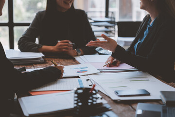 Businesswomen are having a discussion about financial charts and analyzing reports while sitting at a wooden table in the office, collaborating on a project and sharing their expertise