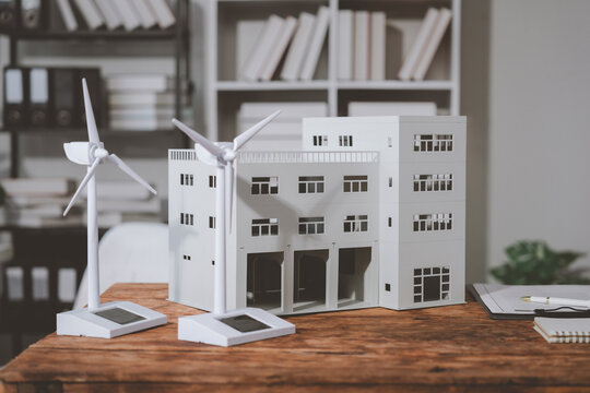 Small scale model of a sustainable building featuring wind turbines and solar panels, positioned on a wooden desk in an architect's office, illustrating renewable energy and eco-friendly design