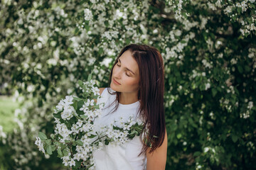 An adult young beautiful female model on the background of blooming apple trees in the garden
