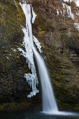 Obraz premium This striking image captures a breathtaking waterfall, adorned with ice formations, cascading down rocky terrain, showcasing the raw power of nature in a serene setting.