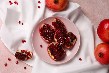 Plate with pieces of fresh pomegranate and seeds on pink background
