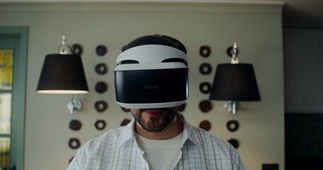 A stylish man in casual clothes takes off a virtual reality headset and looks into the camera with a smile, front view