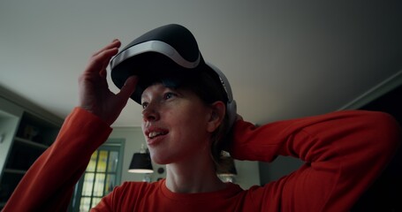 A woman in casual clothes puts on a virtual reality headset and starts moving her hands, turning in different directions, standing in a stylish home interior