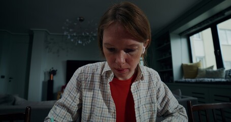 A young woman in casual clothes makes notes in a notebook, and uses a laptop while sitting at a...