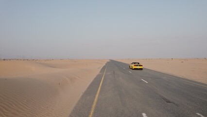 The drone catches up with a yellow convertible with three men riding in it on a road in the desert...