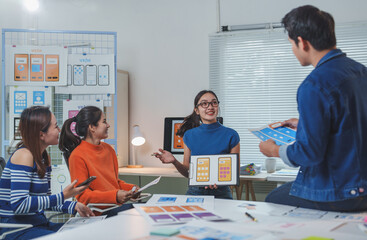 Asian team of ux ui designers discussing mobile app interface wireframe design on desk in modern...