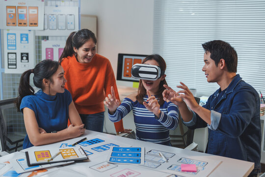 Asian software developers team testing virtual reality application in modern office, woman wearing vr headset interacting with virtual reality world, colleagues looking and giving advice - Powered by Adobe