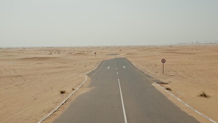 Drone view of an asphalt road in the middle of the desert, covered with sand