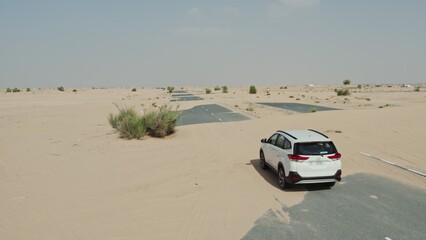 Drone view of a white SUV driving along a modern paved road covered with desert sand © m-art
