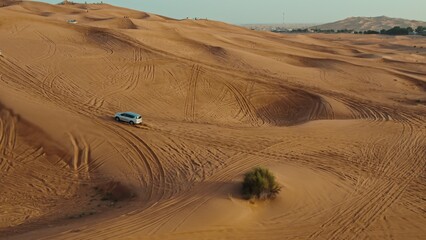 Cars drive off-road on the red sand dunes of the desert with sparse vegetation among the sand, drone video