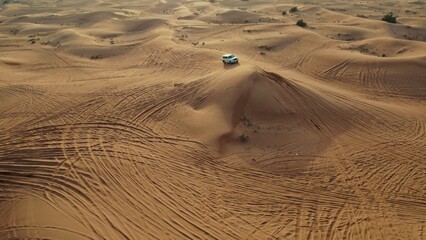 The car drives off-road sand dunes leaving footprints in the sand. Aerial view from a drone