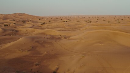 A bird's-eye view from a drone of sand dunes with traces of cars engaged in off-road driving, and sparse vegetation among the sand