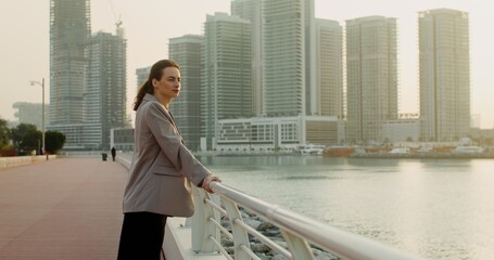 A young woman in business clothes stands on the Persian Gulf embankment overlooking the Dubai city...