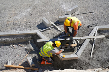 Top view of workers installing concrete road curbs around water drainage at highway construction site