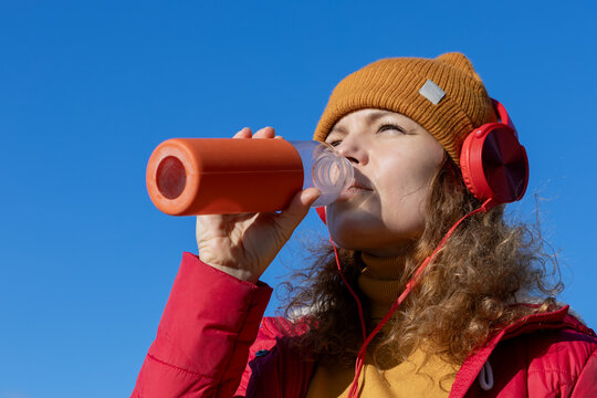 portrait of a woman with headphones drinking water against blue sky