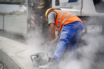Worker cutting groove between concrete and road curbs with smoke at highway construction site