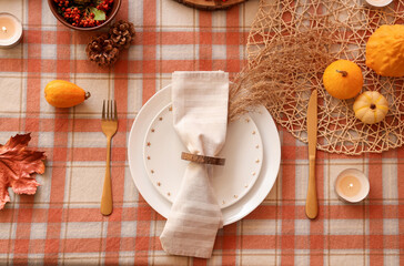 Autumn table setting with folded napkin, golden cutlery and pumpkins, closeup