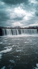 A wide waterfall cascades over a rock dam under cloudy skies