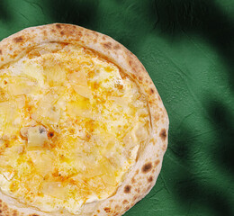 Pizza topped with cheese and pineapple on a green background