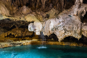 This image showcases a serene underground pool beneath rocky formations, featuring a gentle...