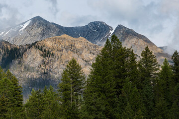 A breathtaking view of majestic mountains capped with snow, standing tall against a lush green forest, capturing the awe-inspiring beauty of nature's grandeur.