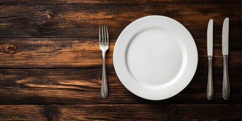 Elegant white dinner plate centered on a rustic wooden table with a silver fork to the left and a silver knife to the right, creating a classic setting.