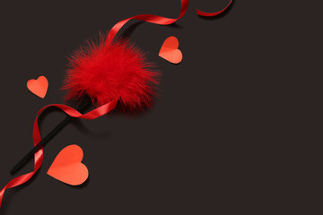 Composition with feather stick from sex toys, paper hearts and red ribbon on dark background....