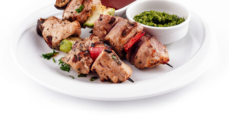 Grilled meat and vegetables on skewers served on white plate with sauces
