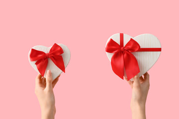 Female hands with gift boxes in shape of heart on pink background. Valentine's Day celebration