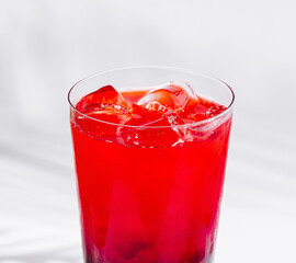 Glass of red cocktail with ice cubes on white background