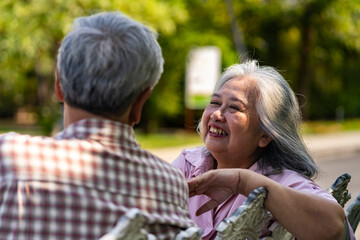 Asian senior couple talking and smiling while sitting on bench in park
