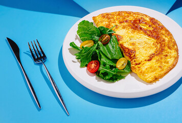 Fresh vegetable salad and omelet on white plate with cutlery